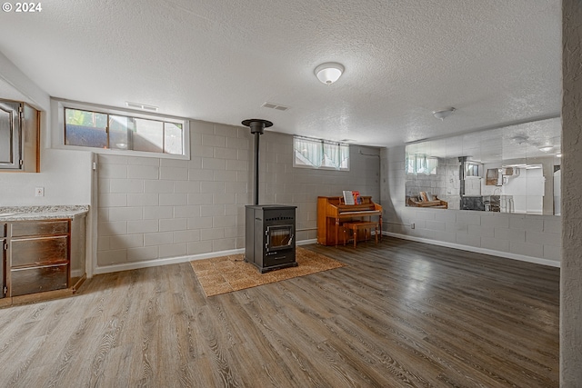 basement with plenty of natural light, wood-type flooring, a wood stove, and a textured ceiling