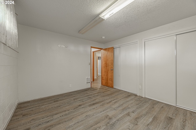 unfurnished bedroom featuring hardwood / wood-style flooring, ceiling fan, a textured ceiling, and multiple closets