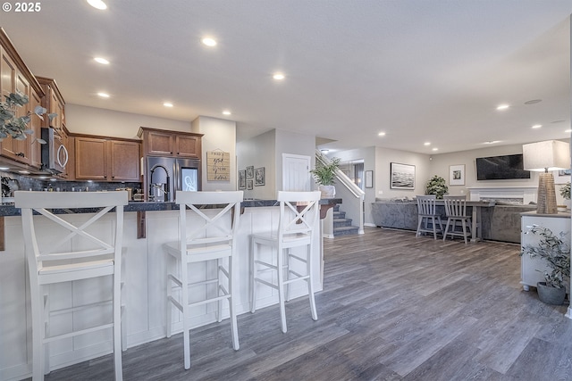 kitchen featuring a breakfast bar, open floor plan, dark wood-style floors, appliances with stainless steel finishes, and brown cabinetry