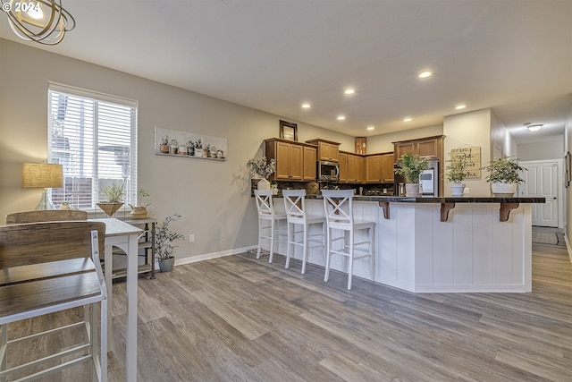 kitchen with a kitchen breakfast bar, light hardwood / wood-style floors, kitchen peninsula, and hanging light fixtures