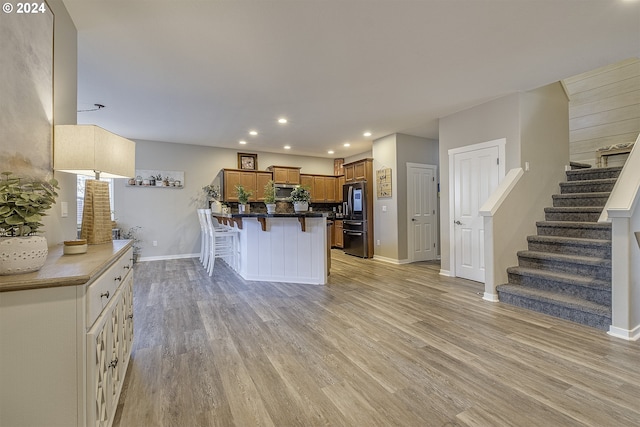 kitchen featuring a kitchen bar, kitchen peninsula, stainless steel refrigerator, and light hardwood / wood-style flooring