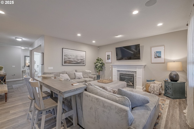 living room with a premium fireplace, recessed lighting, baseboards, and wood finished floors