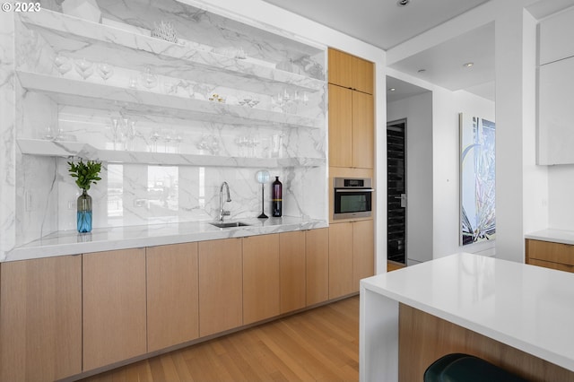 kitchen featuring sink, stainless steel oven, light wood-type flooring, light brown cabinets, and backsplash