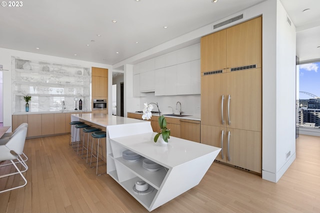 kitchen featuring a large island, white cabinets, a kitchen bar, stainless steel oven, and light wood-type flooring