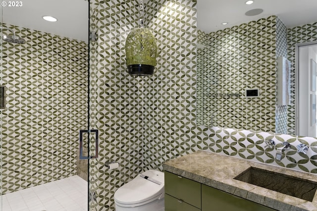 bathroom with a shower with door, vanity, tile walls, and toilet