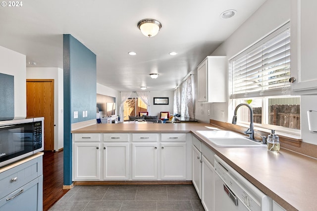 kitchen with white cabinetry, white dishwasher, light countertops, and a sink