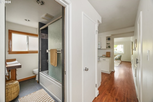 bathroom with hardwood / wood-style floors, bath / shower combo with glass door, and toilet