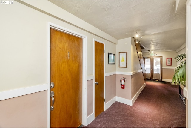 hallway with french doors, dark colored carpet, and a textured ceiling