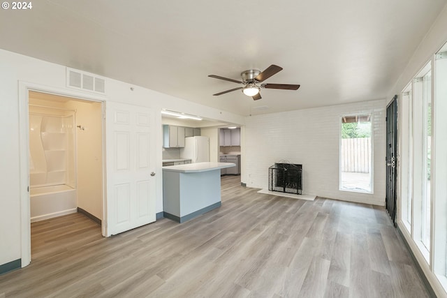 unfurnished living room featuring a brick fireplace, light hardwood / wood-style flooring, and ceiling fan