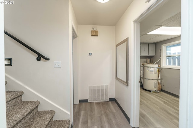 hallway featuring a drop ceiling, secured water heater, and light wood-type flooring