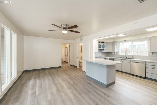 kitchen with sink, appliances with stainless steel finishes, tasteful backsplash, kitchen peninsula, and light wood-type flooring