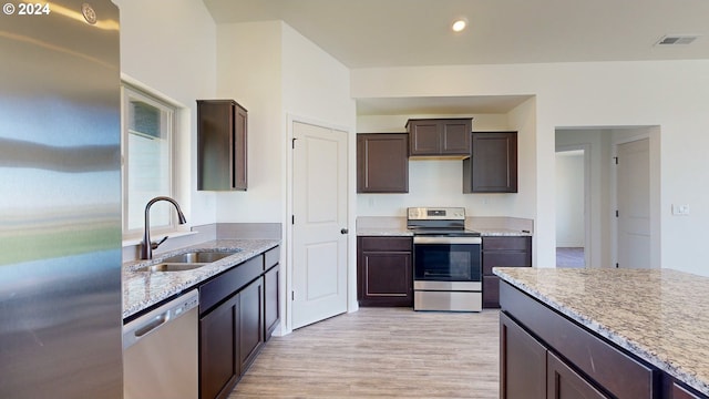 kitchen with sink, appliances with stainless steel finishes, dark brown cabinets, light hardwood / wood-style floors, and light stone counters