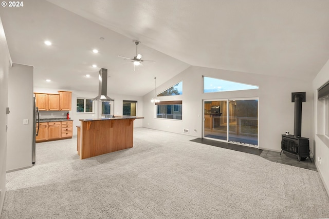 unfurnished living room featuring a wood stove, light colored carpet, high vaulted ceiling, and ceiling fan