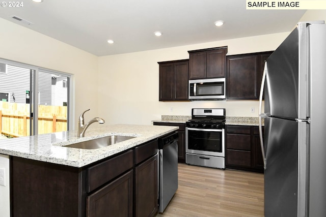 kitchen with dark brown cabinetry, sink, a kitchen island with sink, appliances with stainless steel finishes, and light wood-type flooring