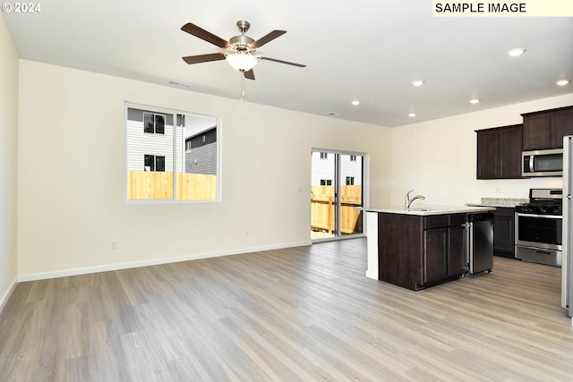 kitchen with ceiling fan, dark brown cabinets, a kitchen island with sink, stainless steel appliances, and light wood-type flooring