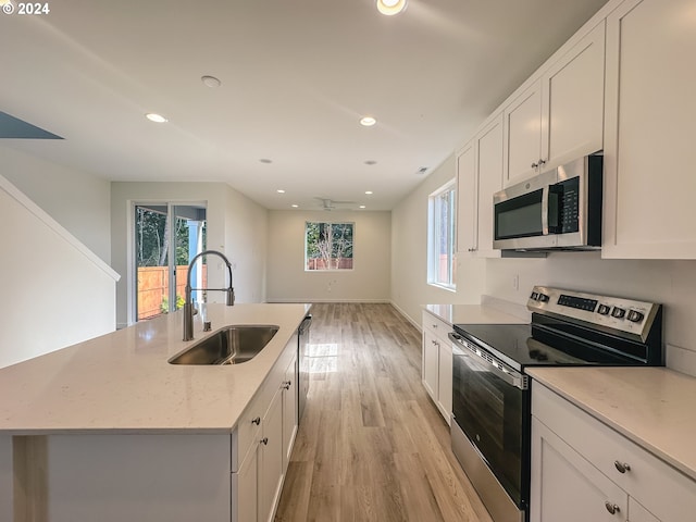 kitchen featuring sink, light stone counters, light hardwood / wood-style flooring, an island with sink, and appliances with stainless steel finishes