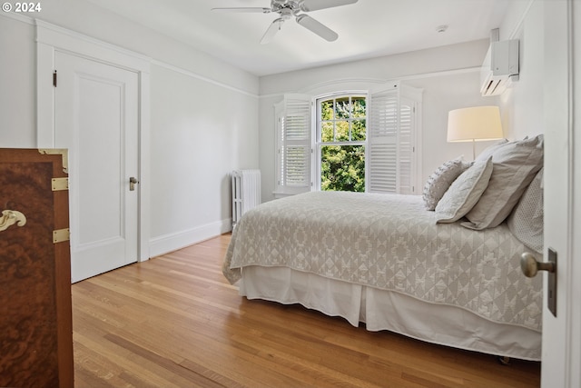 bedroom featuring ceiling fan, radiator, a wall mounted air conditioner, and light hardwood / wood-style flooring