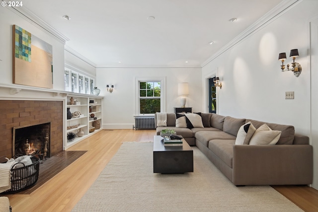 living room with crown molding, radiator heating unit, light wood-type flooring, and a brick fireplace