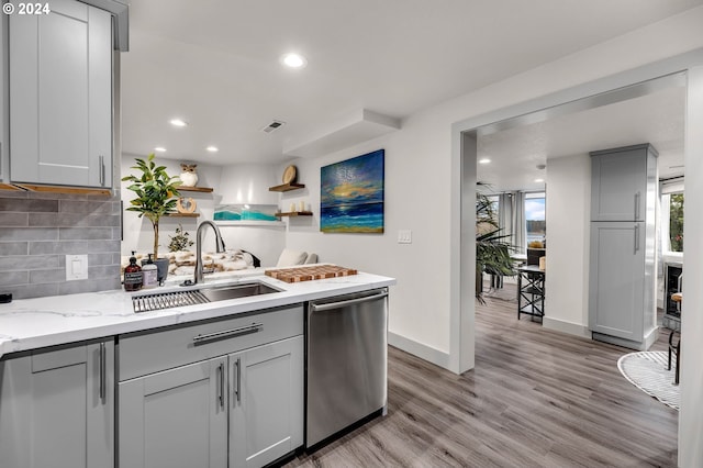 kitchen with light stone countertops, gray cabinetry, sink, dishwasher, and light hardwood / wood-style floors