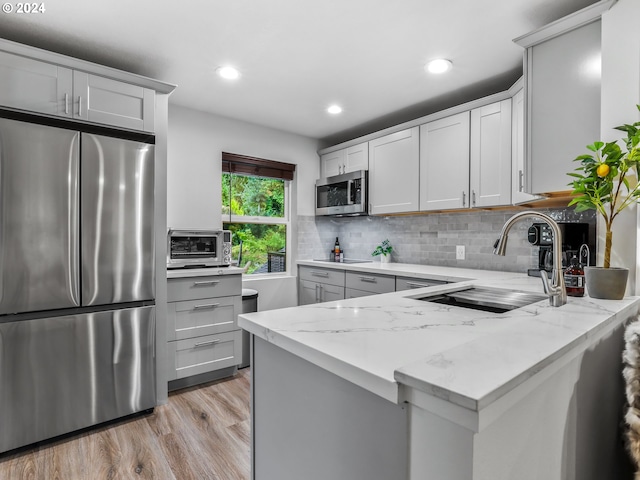 kitchen with sink, light stone counters, backsplash, light hardwood / wood-style floors, and appliances with stainless steel finishes