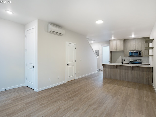 kitchen with light brown cabinets, an AC wall unit, light wood-type flooring, kitchen peninsula, and stainless steel appliances