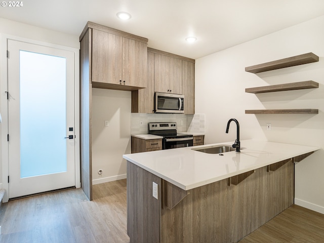 kitchen featuring kitchen peninsula, appliances with stainless steel finishes, light wood-type flooring, and sink