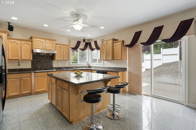 kitchen with gas cooktop, tasteful backsplash, ceiling fan, dark stone countertops, and a center island