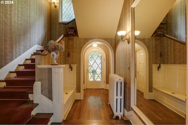 1709 NW Aspen Ave, Portland, OR 97210 - foyer entrance featuring arched walkways, radiator heating unit, stairs, wallpapered walls, and wood finished floors