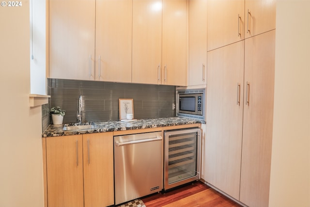 bar with decorative backsplash, appliances with stainless steel finishes, a sink, beverage cooler, and light wood finished floors