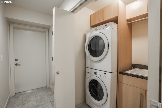 laundry area with sink, light tile patterned floors, and stacked washer and dryer