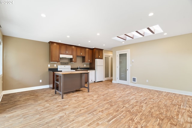 kitchen featuring white appliances, a breakfast bar area, light wood-type flooring, a center island, and a skylight