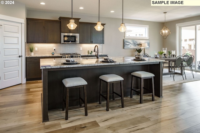 kitchen with dark brown cabinets, light hardwood / wood-style floors, light stone counters, and a kitchen island with sink