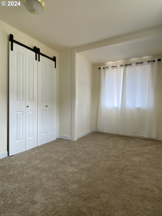 unfurnished bedroom with carpet flooring and a barn door