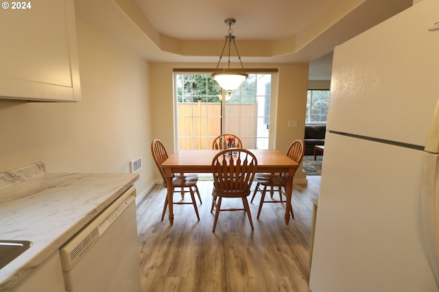 dining area with a raised ceiling, sink, and light hardwood / wood-style floors