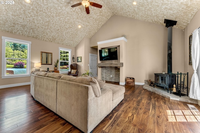 living room with ceiling fan, dark wood-type flooring, a wood stove, and high vaulted ceiling