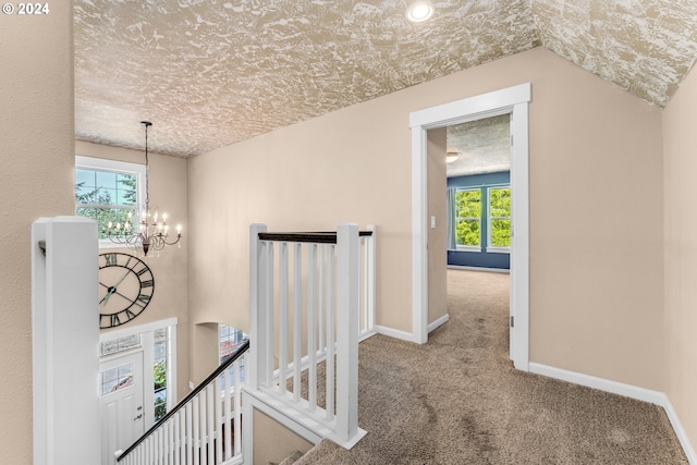 hallway with carpet floors, an inviting chandelier, vaulted ceiling, and a textured ceiling