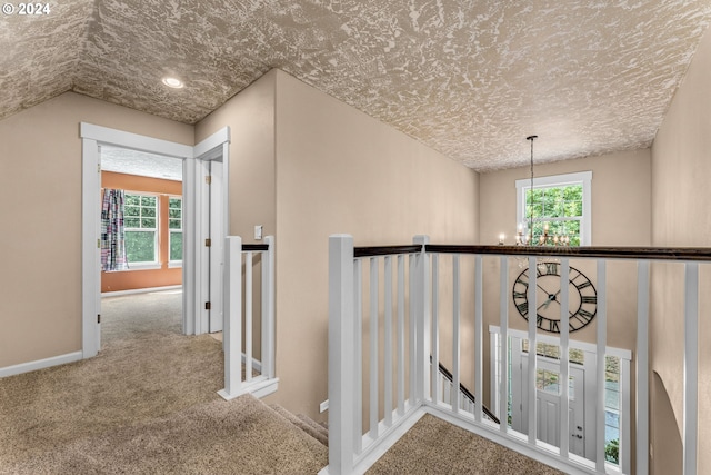 hall with an inviting chandelier, carpet, a textured ceiling, and vaulted ceiling