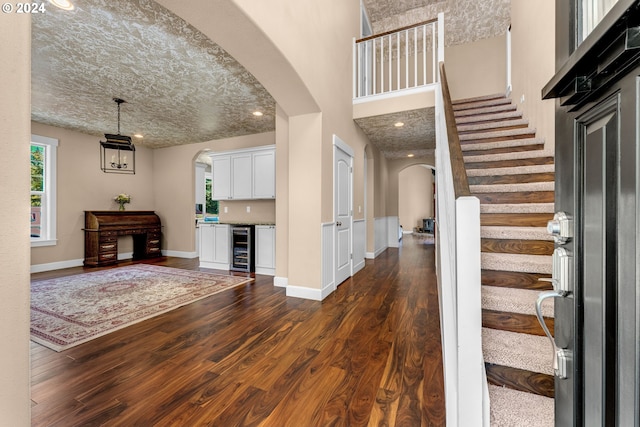 foyer entrance with a textured ceiling, a high ceiling, dark hardwood / wood-style floors, and wine cooler