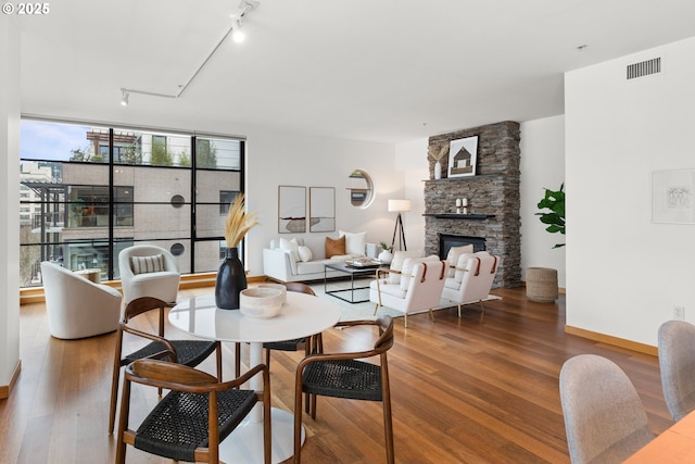 dining area with rail lighting, hardwood / wood-style flooring, and a stone fireplace