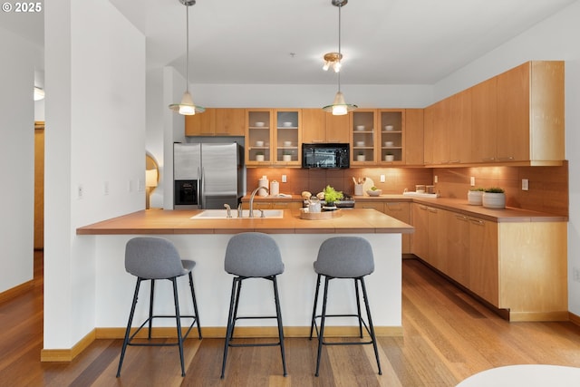 kitchen with a kitchen breakfast bar, tasteful backsplash, stainless steel refrigerator with ice dispenser, kitchen peninsula, and pendant lighting