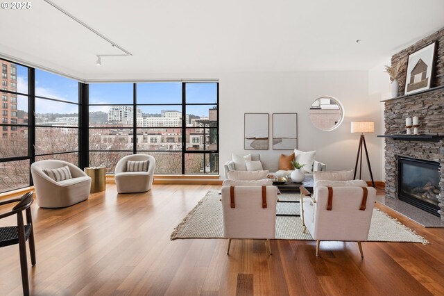 living room featuring a stone fireplace, rail lighting, light hardwood / wood-style floors, and expansive windows