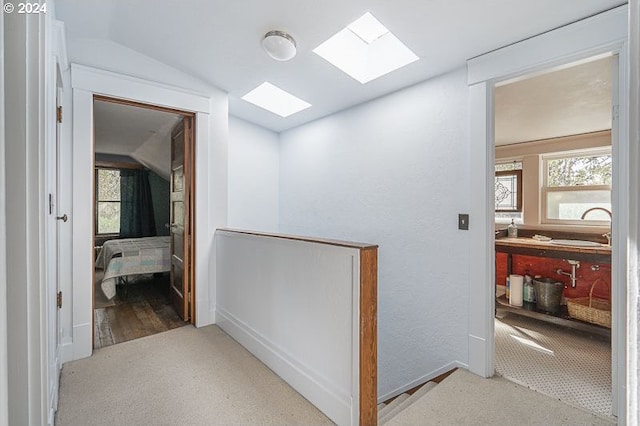hallway with lofted ceiling, a skylight, an upstairs landing, carpet flooring, and a sink