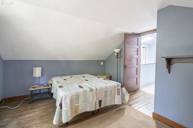 bedroom with wood finished floors, lofted ceiling, and baseboards