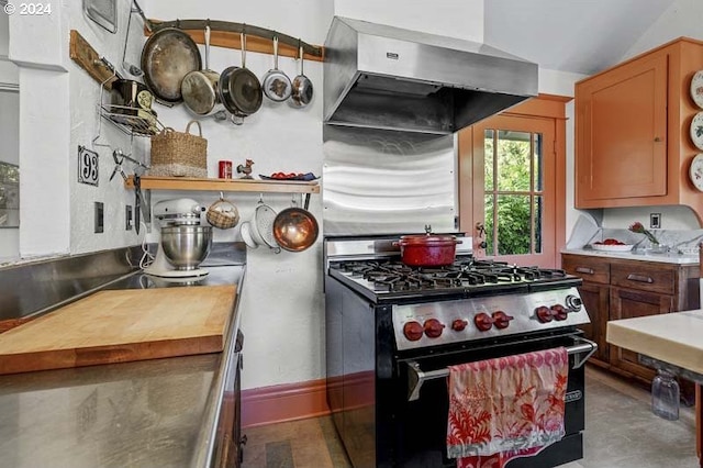 kitchen featuring stainless steel range with gas stovetop, range hood, butcher block counters, and vaulted ceiling