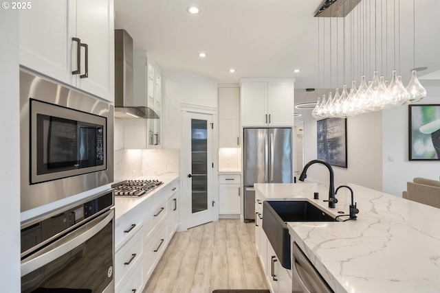 4116 S 16th Way, Ridgefield, WA 98642 - kitchen featuring stainless steel appliances, wall chimney exhaust hood, a sink, light wood-style floors, and white cabinets
