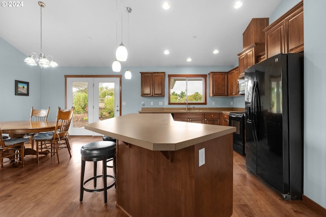 kitchen with decorative light fixtures, a breakfast bar area, a center island, light hardwood / wood-style floors, and black appliances