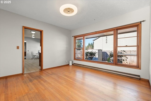 empty room with a textured ceiling, light hardwood / wood-style flooring, and a baseboard heating unit