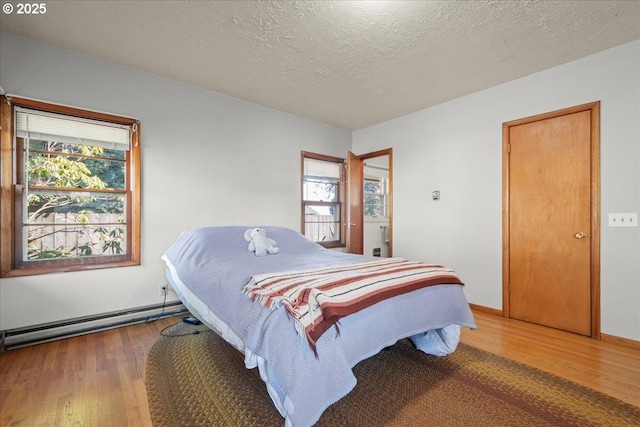 bedroom featuring multiple windows, a baseboard heating unit, and hardwood / wood-style floors