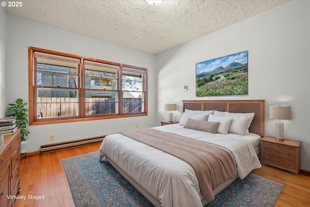 bedroom featuring a textured ceiling, light hardwood / wood-style flooring, and a baseboard heating unit