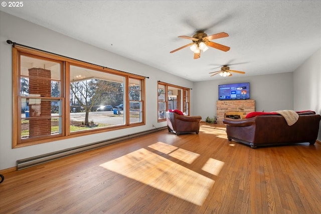 living room with ceiling fan, hardwood / wood-style floors, a fireplace, a textured ceiling, and a baseboard radiator